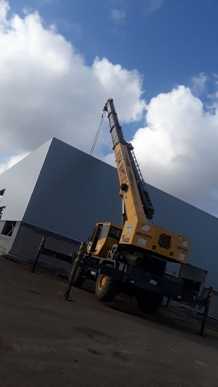Grúa Grove amarilla al lado de galpón industrial - Rosa Mística Construcciones